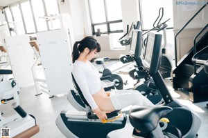 A woman in a white top and white leggings working out in a gym.