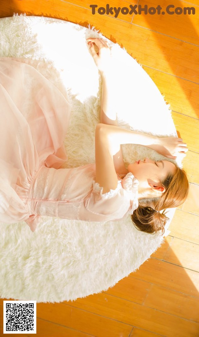 A woman in a pink dress laying on a white rug.