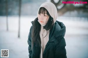 A woman leaning against a tree in the snow.