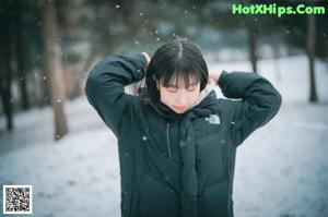 A woman leaning against a tree in the snow.