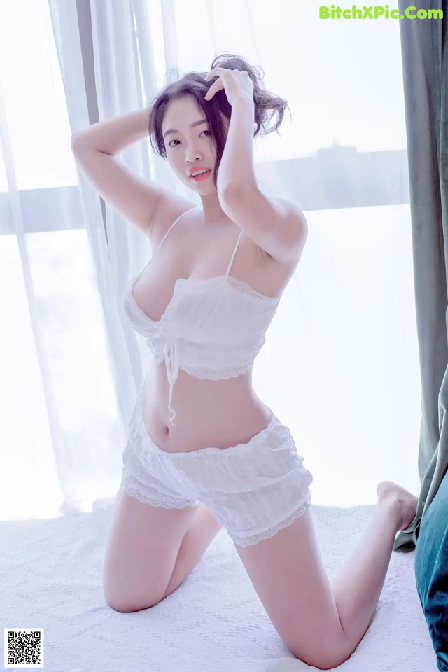 A woman in a white lingerie sitting on a bed.