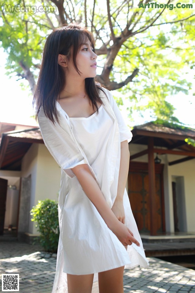 A woman in a white dress standing in front of a house.