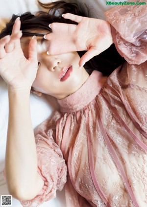 A woman sitting on a bed in a pink robe.