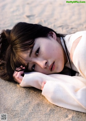 A woman in a white dress laying on the sand.