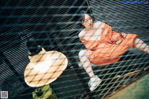 A woman sitting on a chair in an orange jumpsuit.