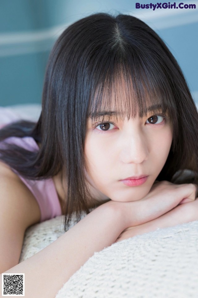 A young woman laying on a bed with her hand on her chin.