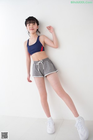 A woman in a blue top and gray shorts leaning against a wall.