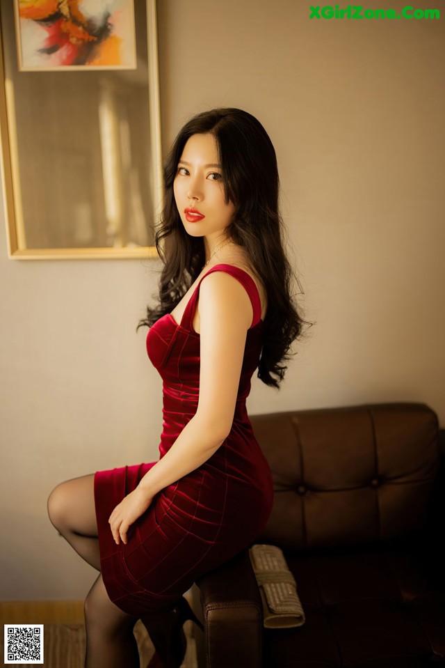 A woman in a red dress sitting on a brown couch.