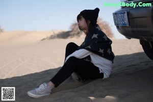 A woman sitting in the sand with a blanket over her head.