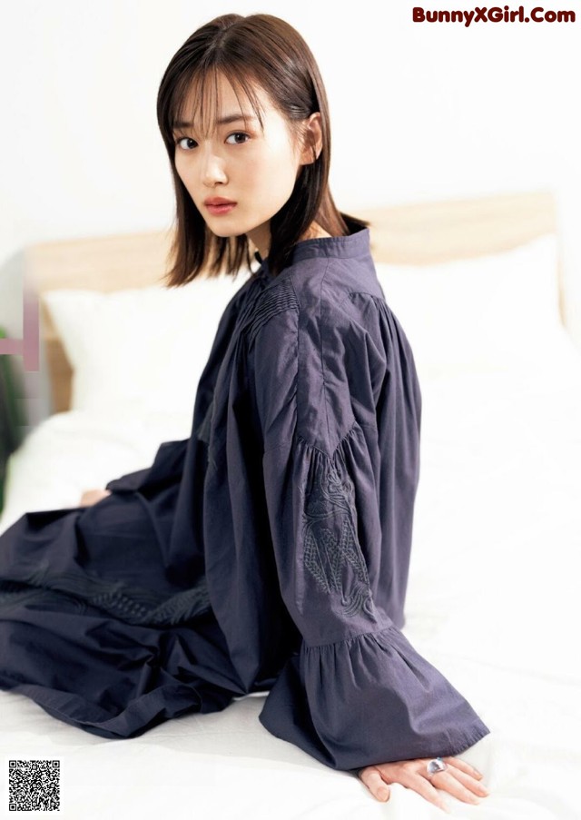 A woman sitting on a bed wearing a black dress.