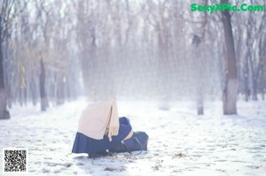 A woman in a white sweater and blue skirt standing in the snow.