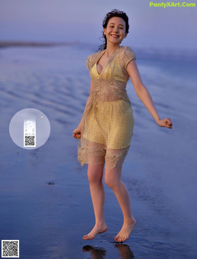A woman in a yellow dress walking on the beach.