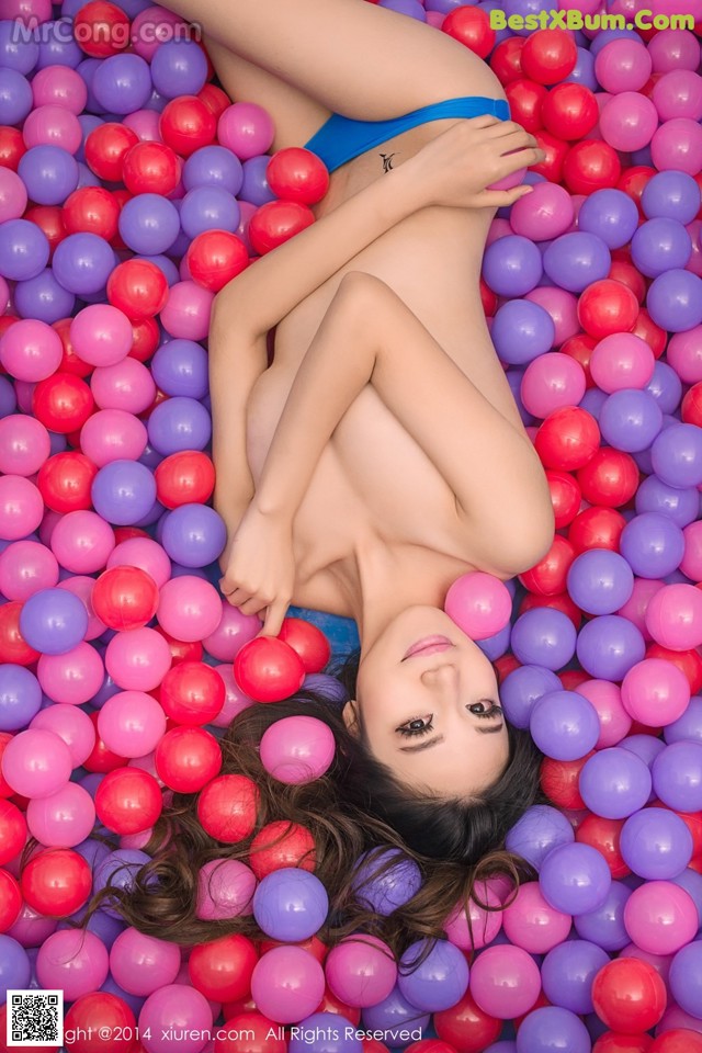 A woman laying in a ball pit of pink and purple balls.