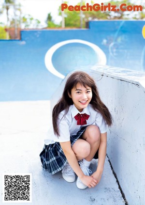 A young girl in a school uniform crouching down on the ground.