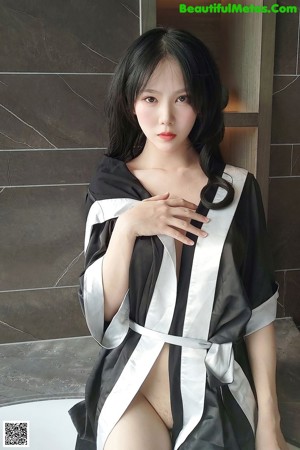 A woman in a black and white robe sitting on the floor.